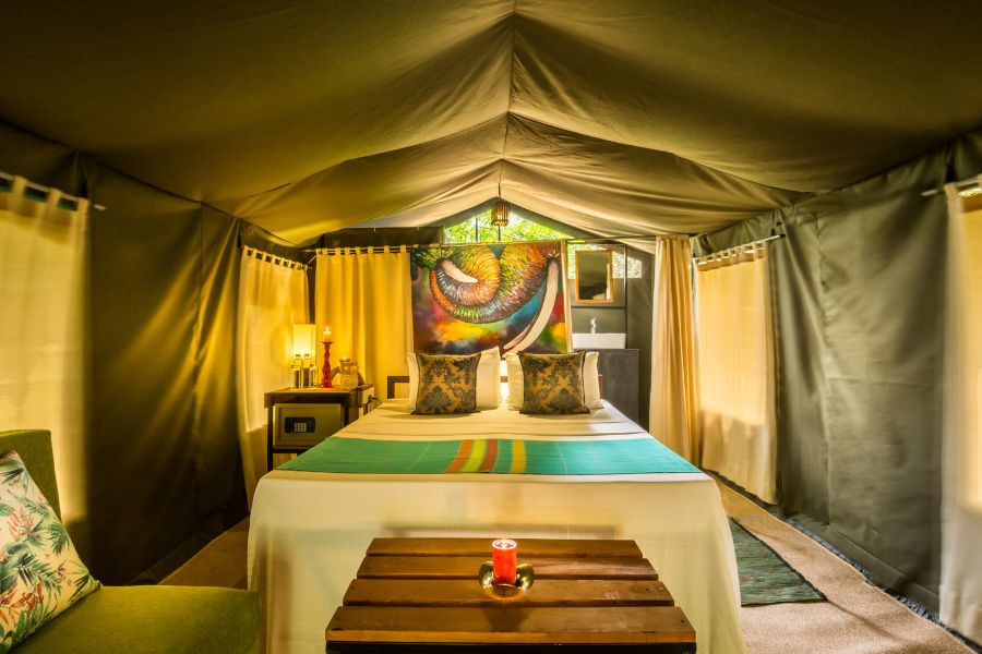 A bedroom tent with a made-up bed, cushions and a patterned wall hanging under the canvas