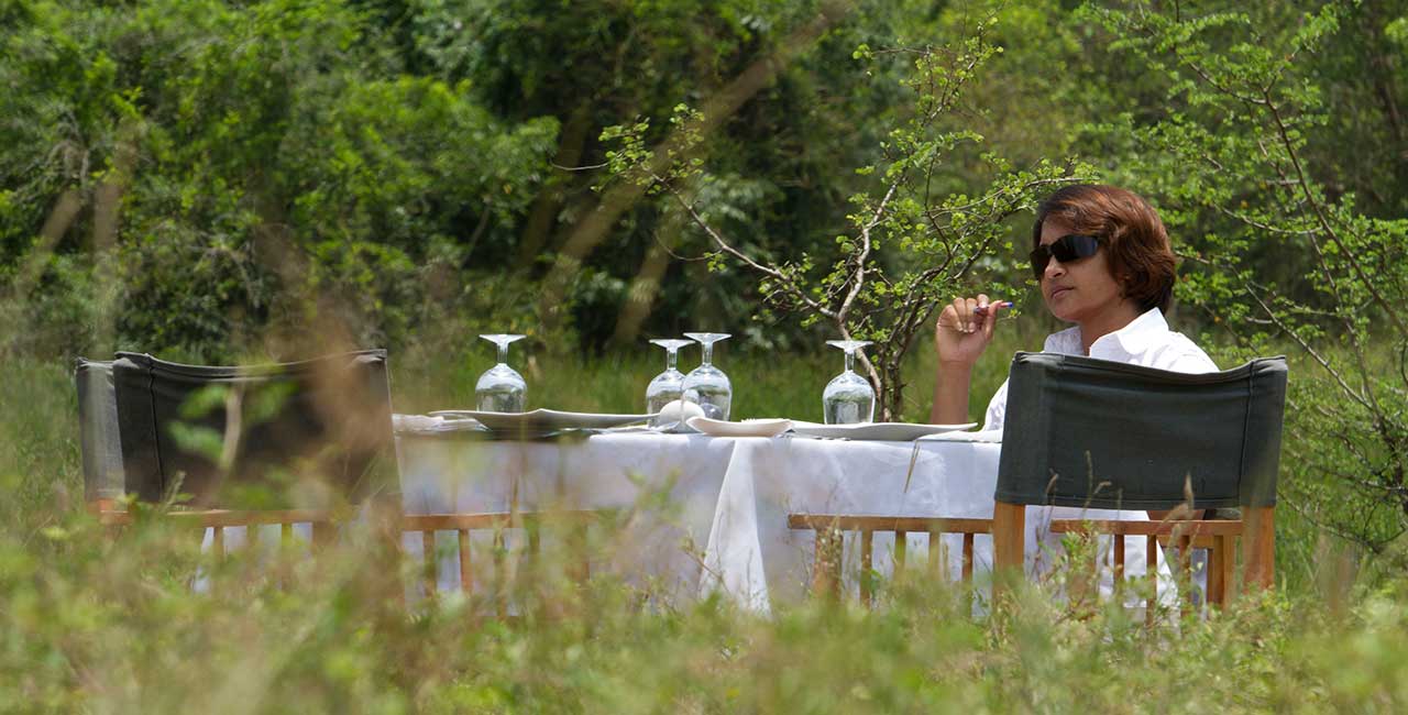 A guest at a table laid with glasses and white linen in the bush.